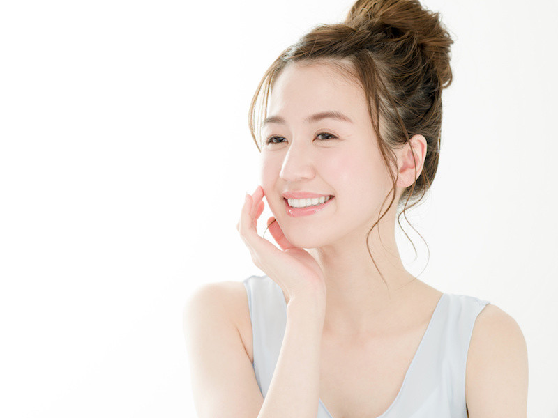 顔に右手を添えてほほ笑むお団子ポニーテールの女性